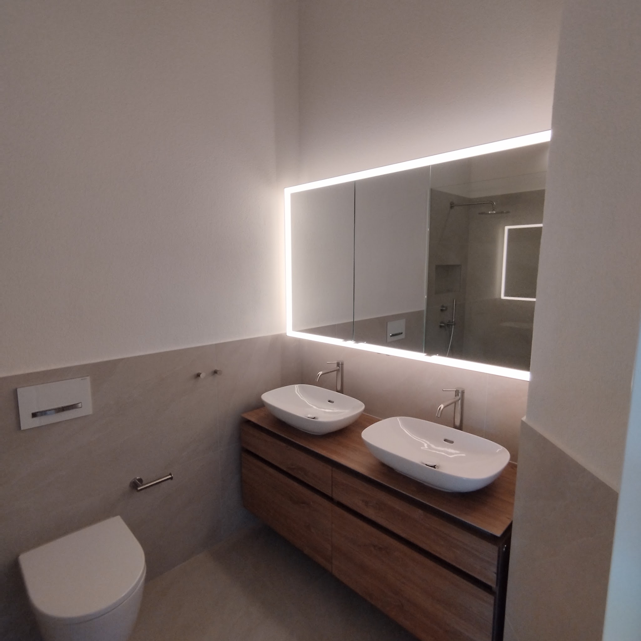 Badezimmer mit Doppelwaschtisch und beleuchtetem Spiegel
